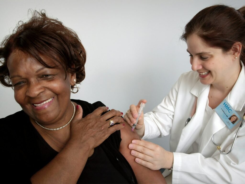 An older woman smiles while a nurse attends to her