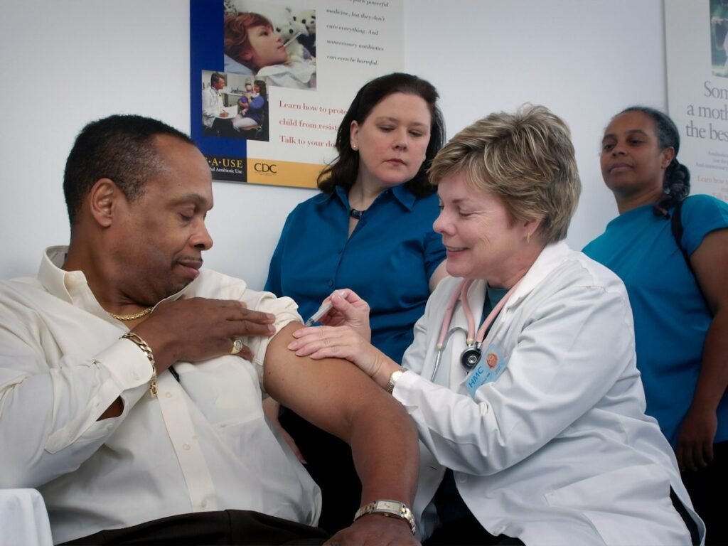 An older man supported by a small team of health workers